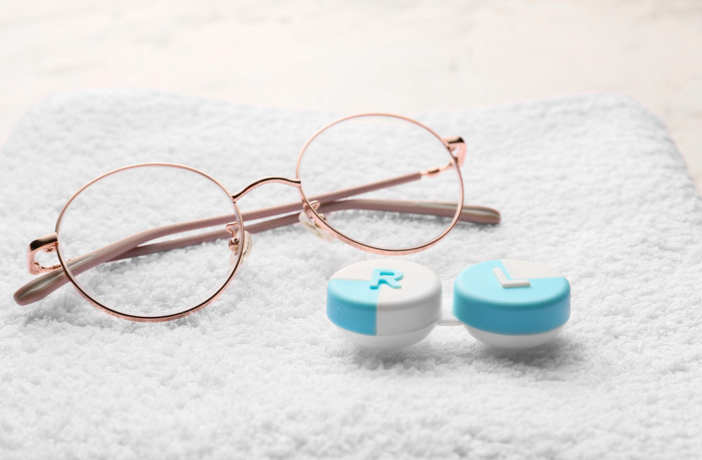 Glasses and contact lens box on white towel.
