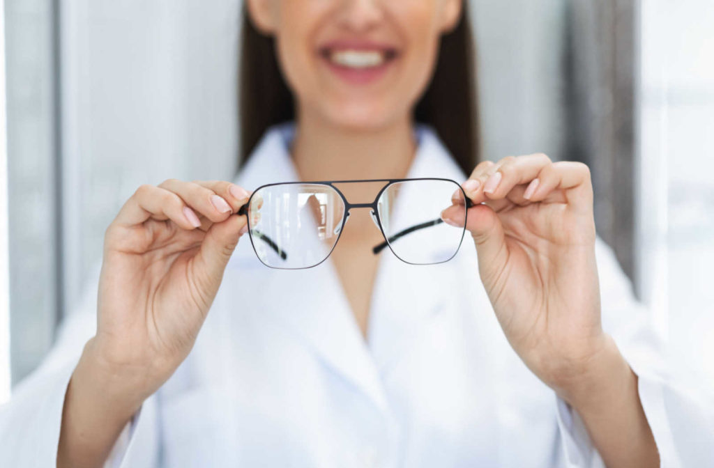An optometrist smiling while holding a pair of glasses out in front of her