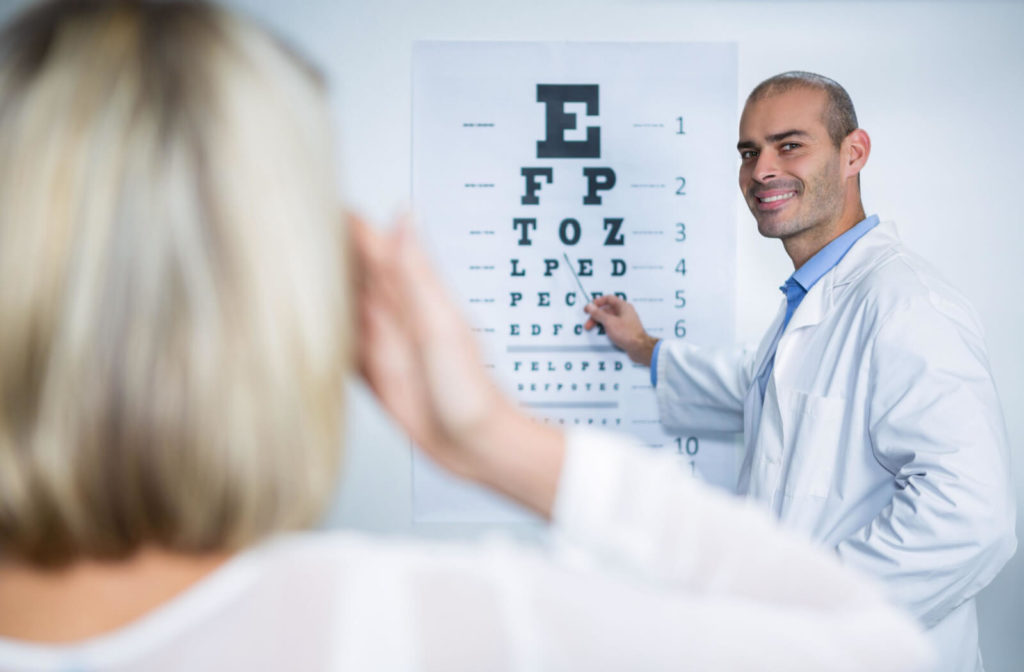 A male optometrist is pointing a letter on a Snellen Chart in examining the patient's eye vision.