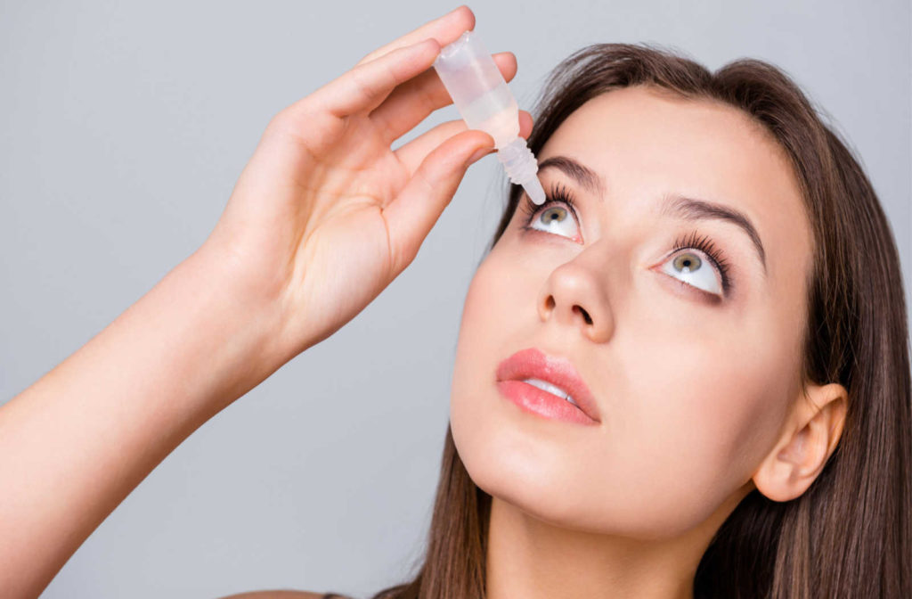 A woman looking up holding a bottle of prescription eye drops to use in her eye
