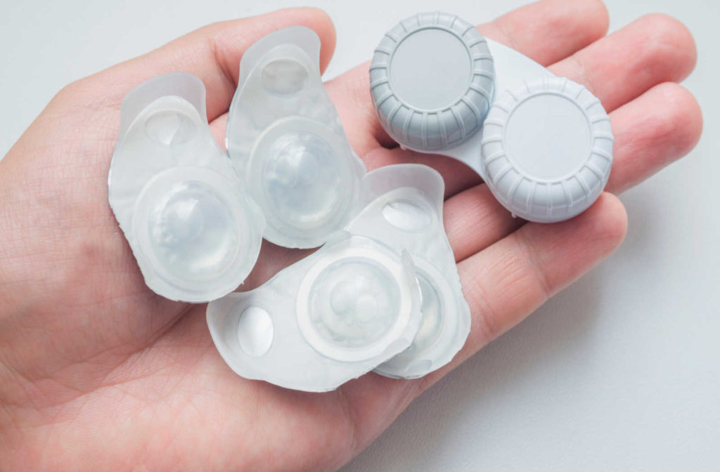 A hand holding a contact lens case and contact lens blister packs