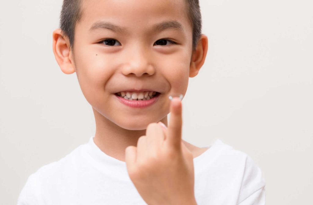 A young boy smiling while holding a gas permeable contact lens on his finger