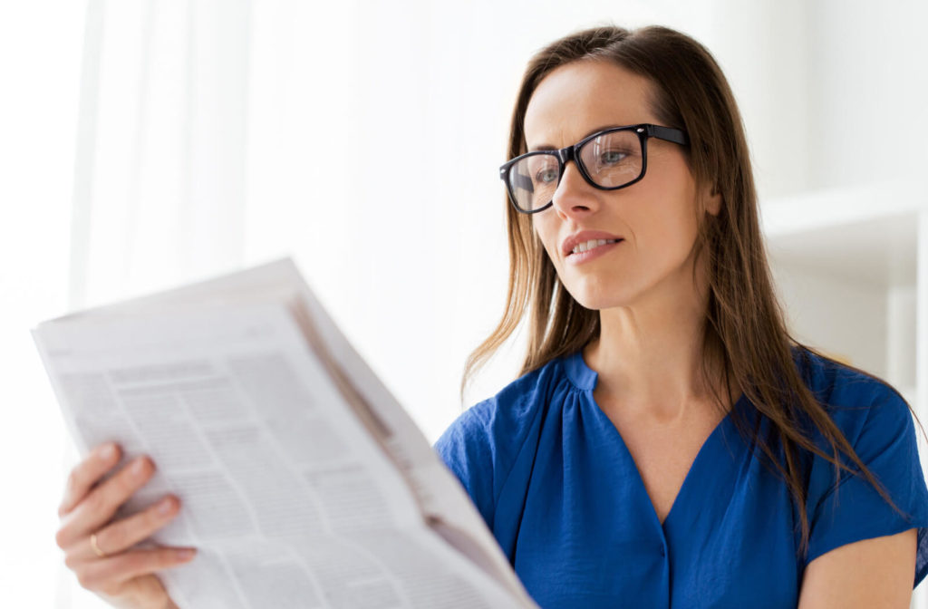 A woman with reading glasses reading a newspaper.