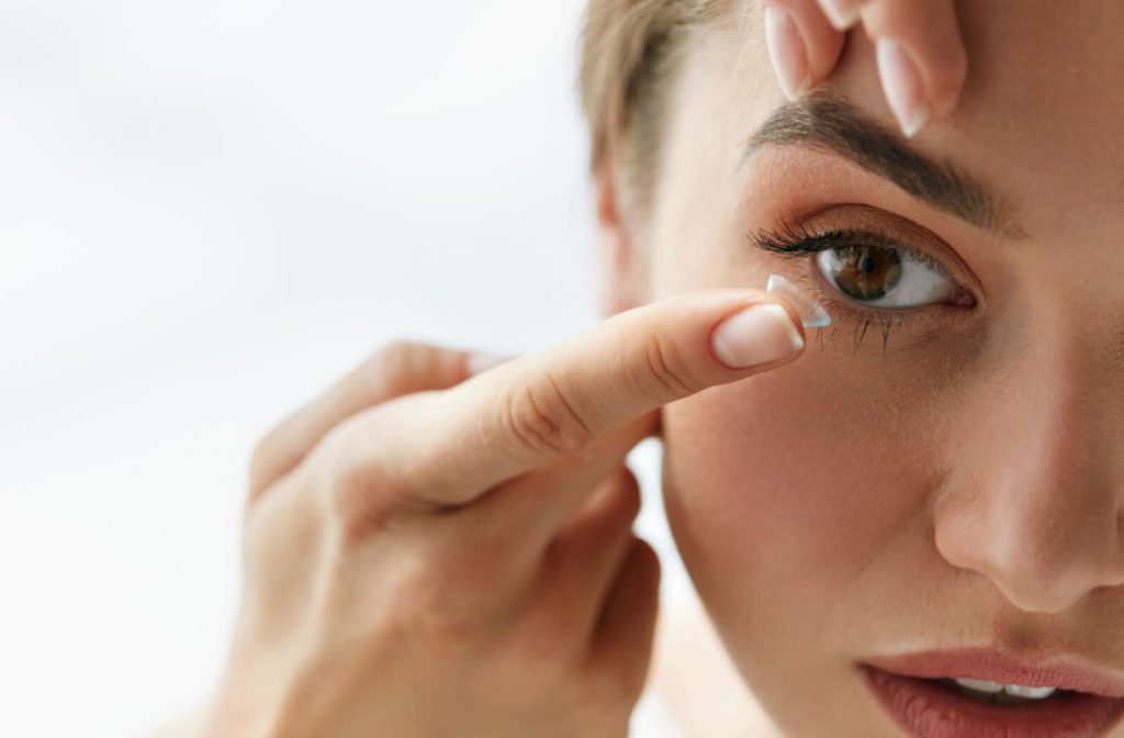 A woman using her left index finger to pull her right eyelid up while she puts a contact lens in her right eye with her right index finger.