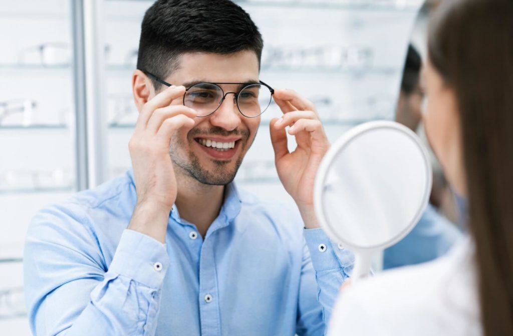 A young man trying on glasses at an optical store while being assisted by an optometrist.
