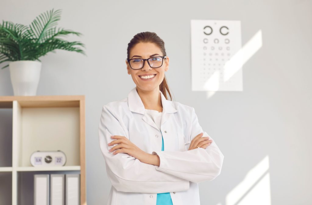 A female optometrist in a clinic, crossing her arms and smiling while looking directly at the camera.