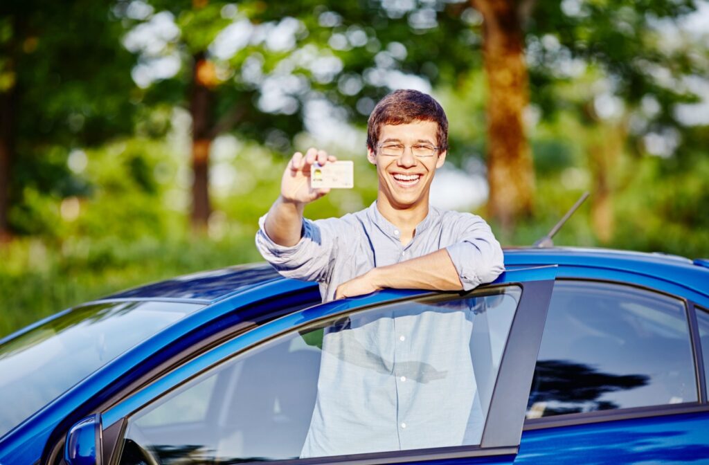 A young driver smiles while holding his driver's license.