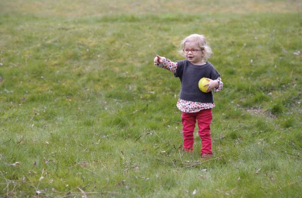 Child with glasses playing outside after her first eye exam at an optometrist.