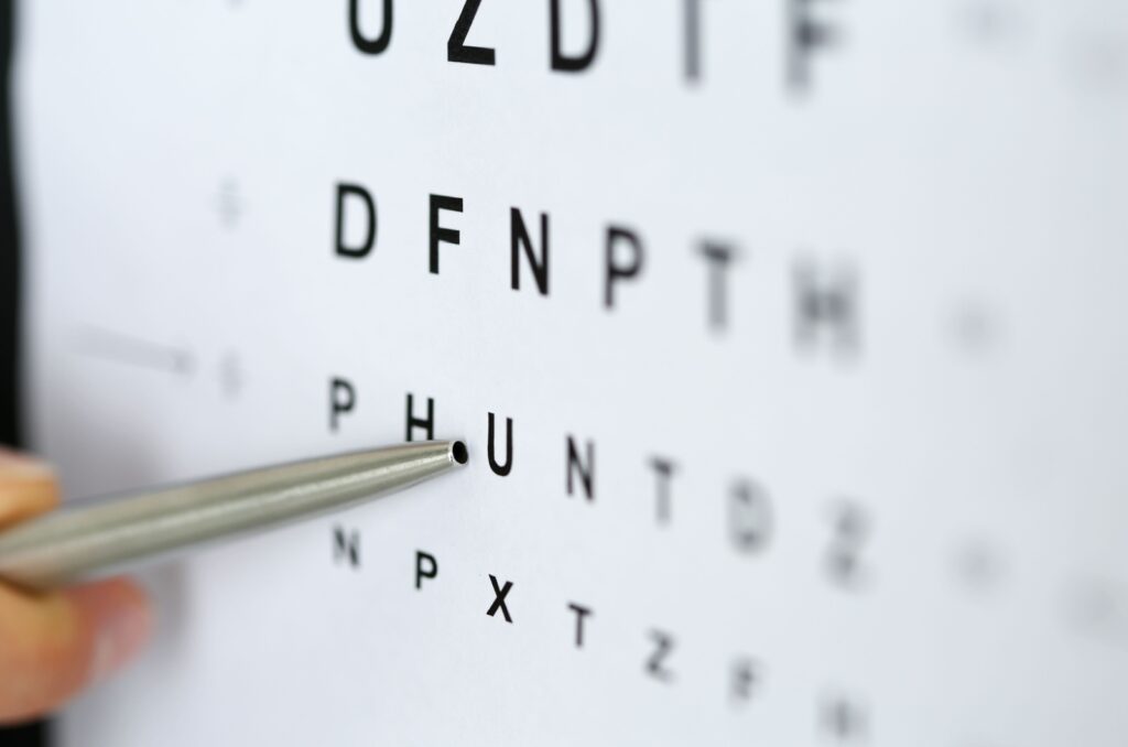 A close up image of a silver pen pointing to a letter on an eye chart.