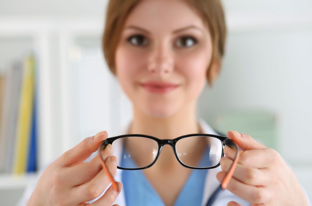 A smiling female optometrist holding up a pair of eyeglasses in their hands.