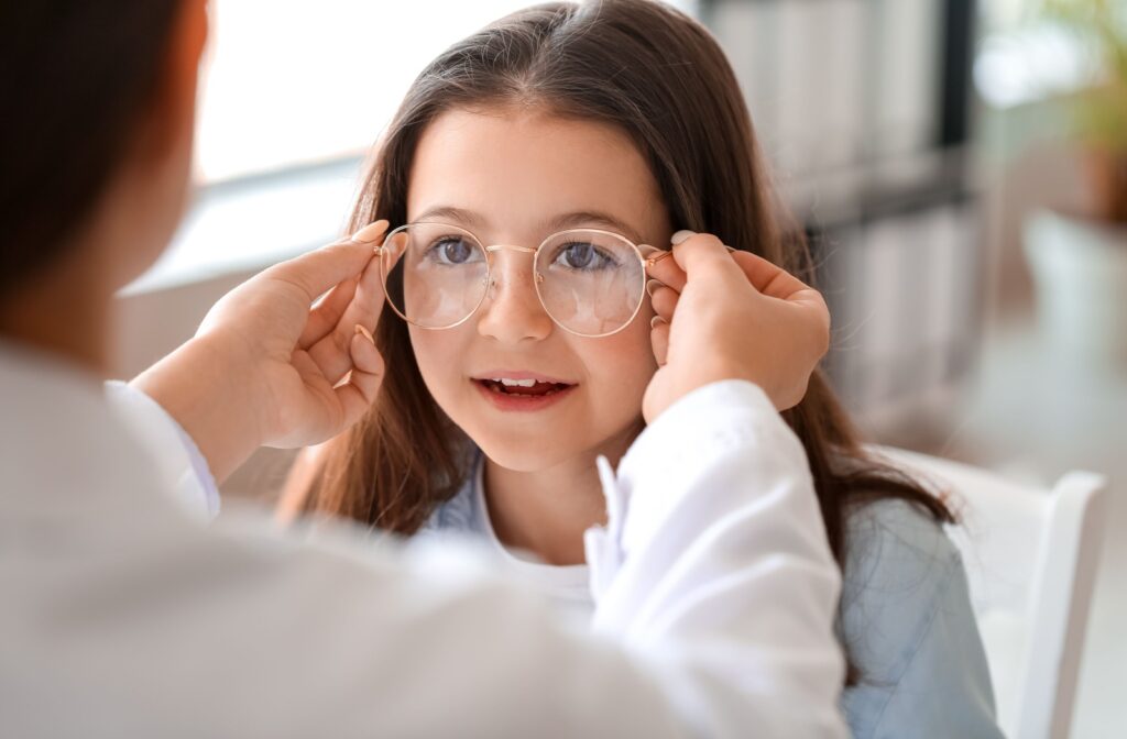 An optometrist placing corrective glasses for myopia on a child's face.