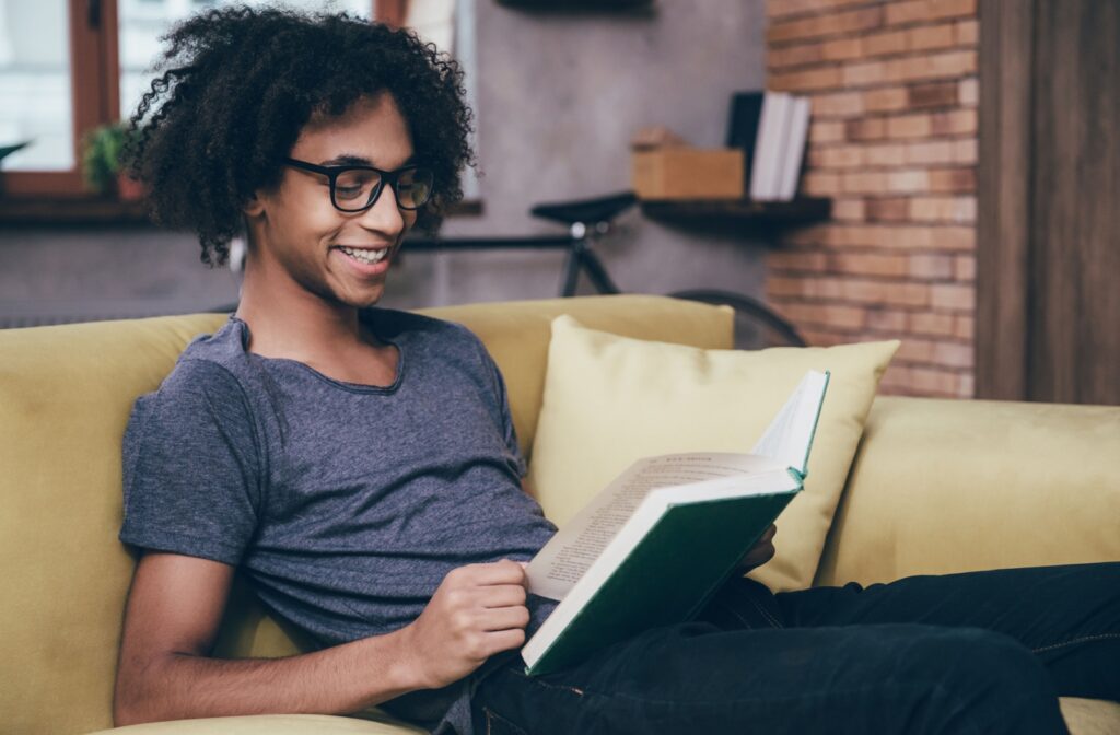A person wearing Neurolens glasses sitting on a couch, reading a book