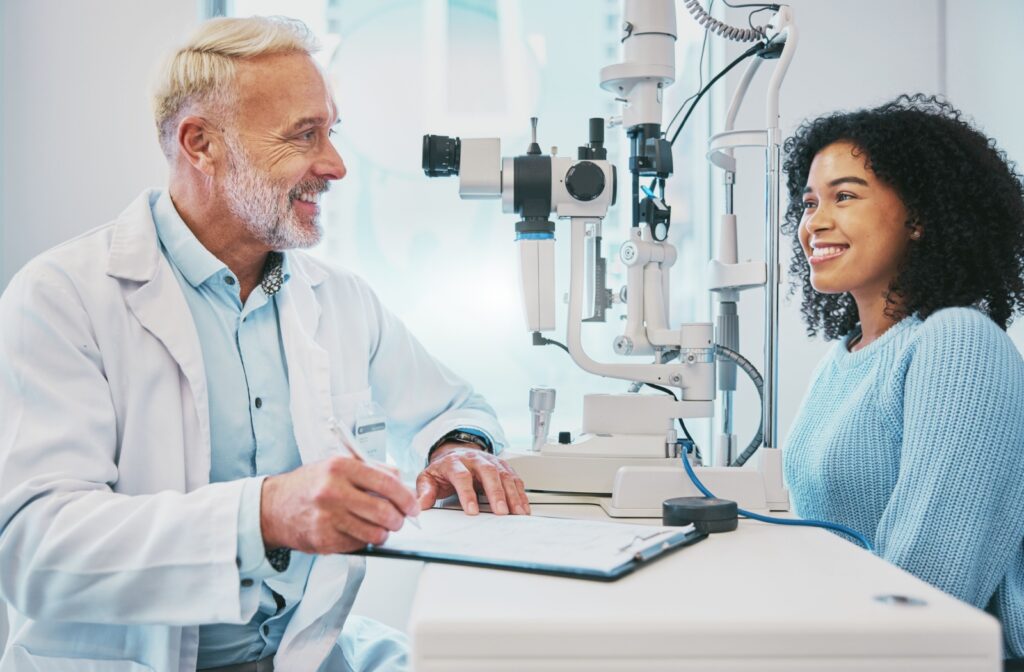 An eye doctor sitting across from a patient, smiling while performing an eye exam.
