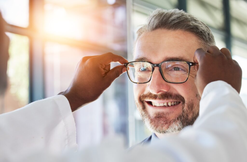 An optician placing a new pair of fitted glasses onto a patient at an optometrist's office.